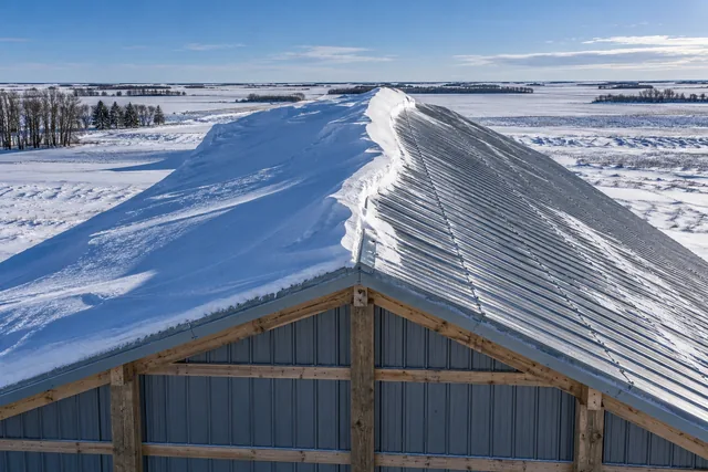 Pole barn roof after a blizzard showing deep drift accumulation on the leeward side and scoured panel on the windward side