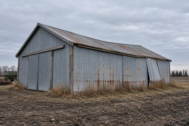 Older pole barn with a sagging ridge line, faded chalked steel panels and rust weeping from fastener heads