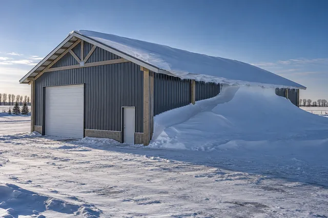 Pole barn roof in deep winter with a large wind-driven drift banked up the leeward wall above door height